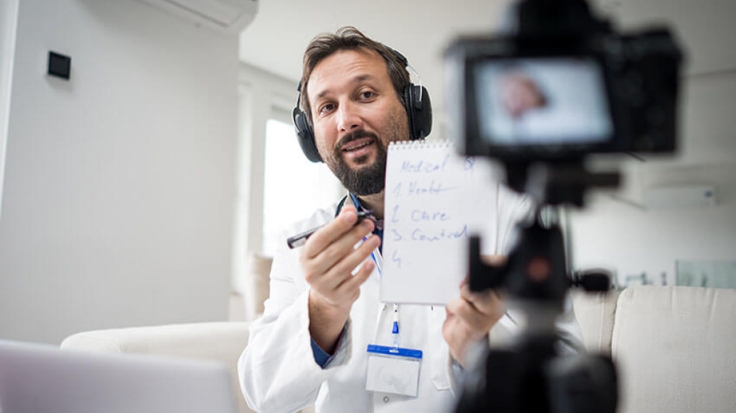 Doctor talking into camera in clinic holding notepad