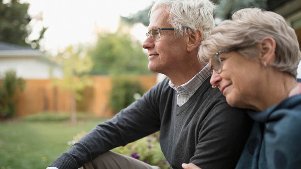Older woman leaning on shoulder of older man sitting outside.