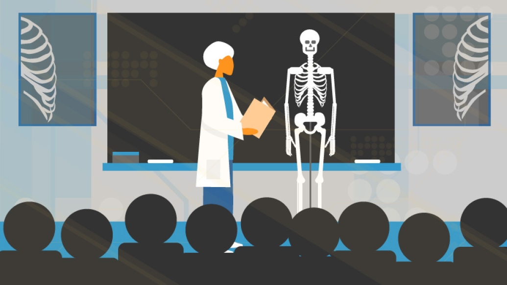 Teacher with white hair in classroom teaching students with skeleton in front of blackboard