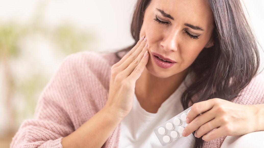 woman tooth pain holding pills in pink shirt