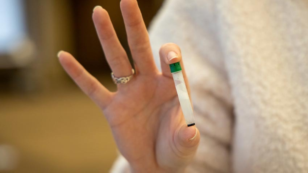 woman holding clear vial with green lid in two fingers