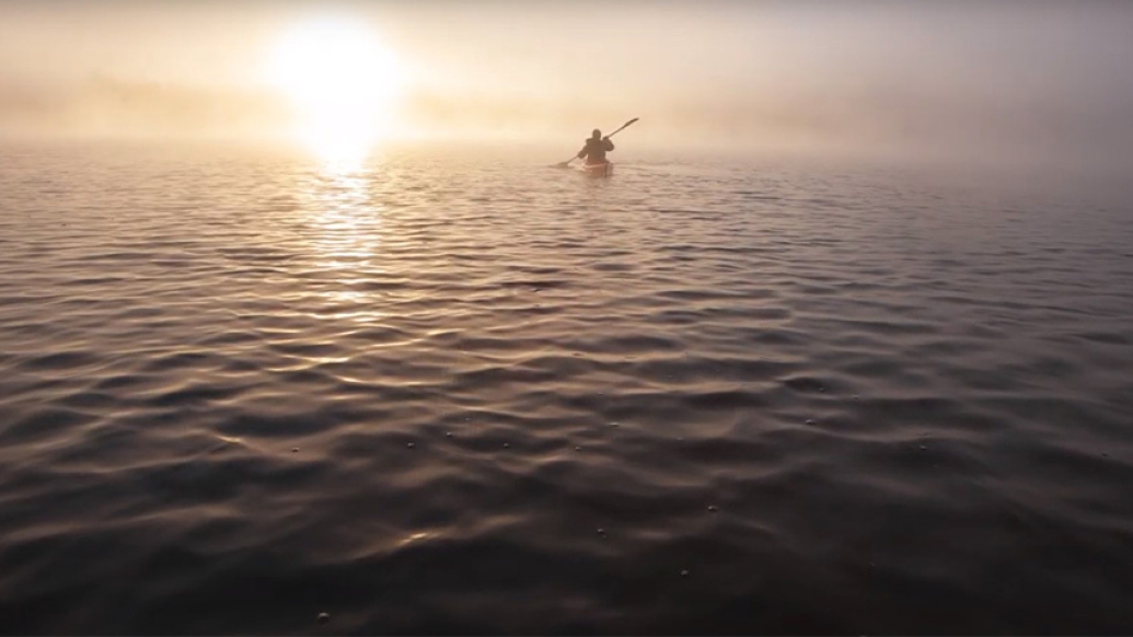 man paddling in boat on open water with sun