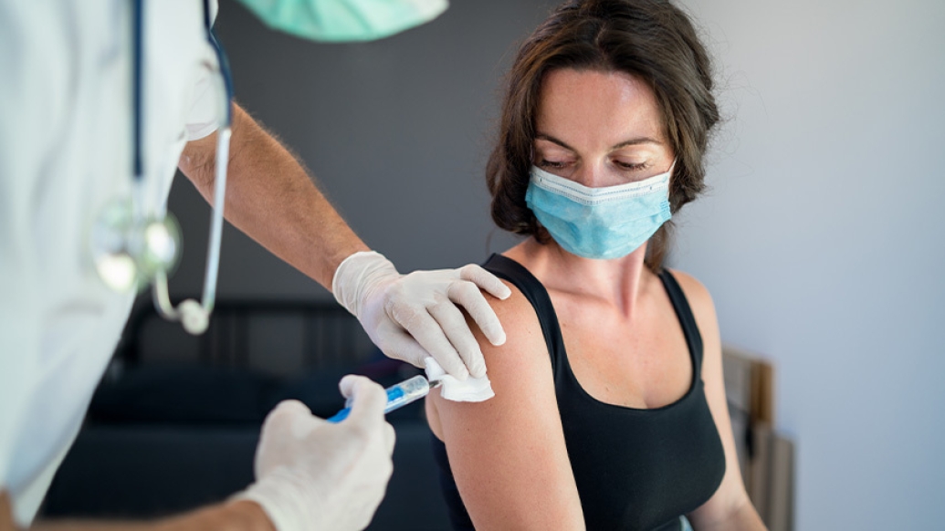 white woman getting vavvine in arm with mask on from practitioner with white gloves and stethoscope