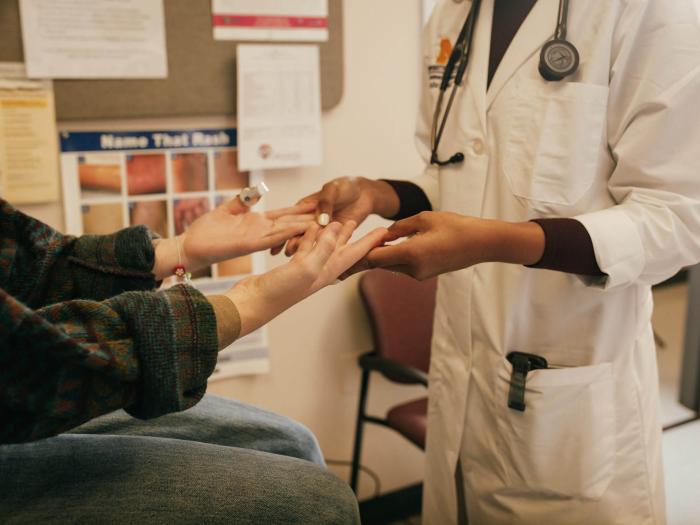Hands and arms of white seated female patient and standing Black doctor