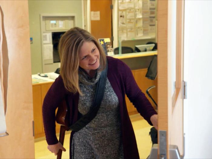 Woman with guitar smiling while peeking around the corner of a patient room
