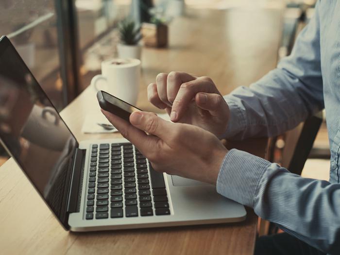man in blue button-down shirt holding a mobile phone in front of a laptop