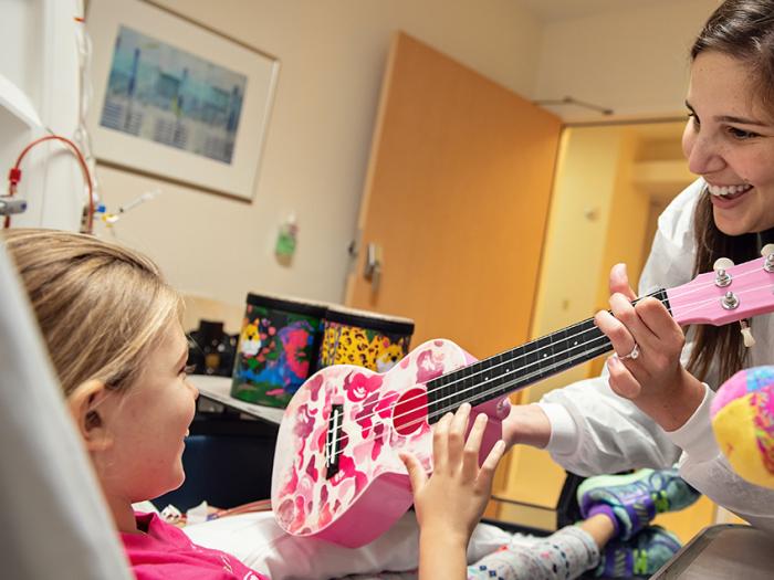 woman handing female pediatric patient laying in a hospital bed a pink guitar