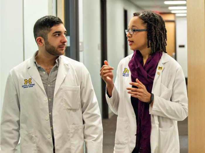 Two medical students, one male and one female, talking while walking down a hallway