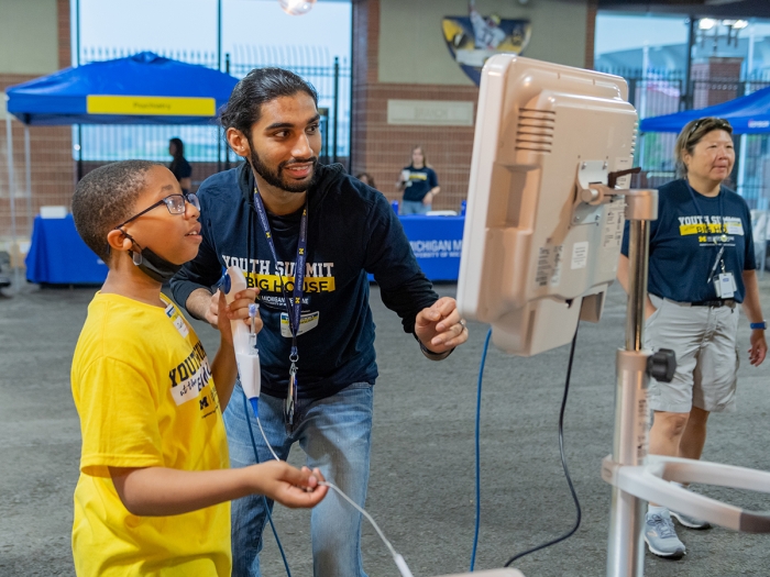 Young diverse man with beard helping Black boy in front of monitor, both wearing Youth Summit t-shirts
