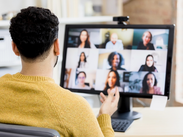 Man with dark hair and beard shown from back looking at virutal meeting on computer screen