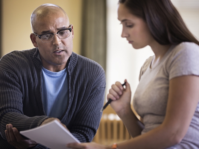Bald man pointing at paper a younger woman with long dark hair is holding
