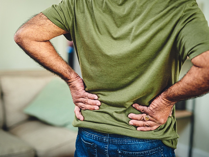 The back of a man in a green shirt with his hands on his lower back