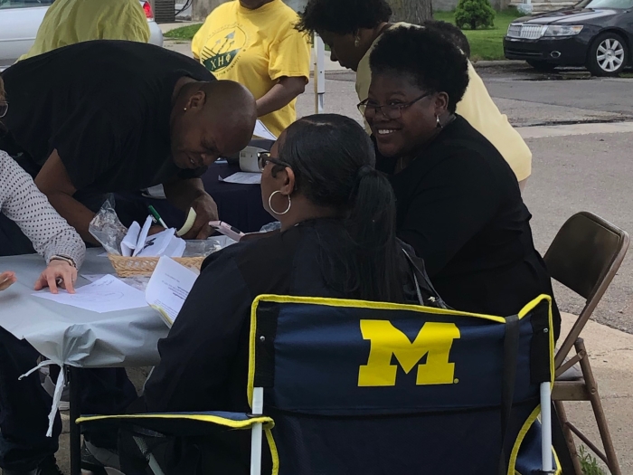 Group of people seated at outdoor table with block M logo on back of chair