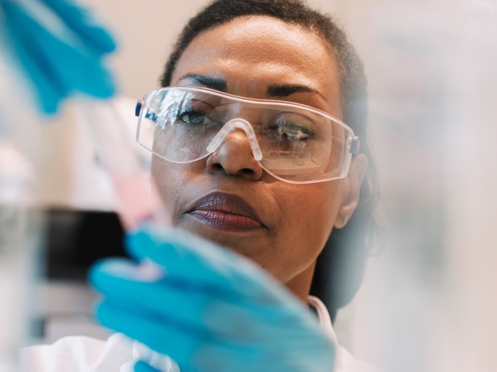 woman wearing protective eye glasses examining a vile of pink liquid