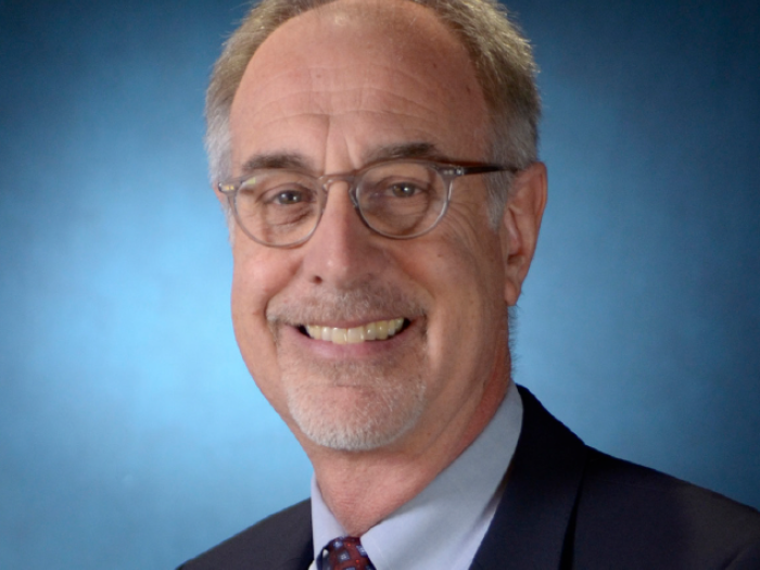 Professional portrait of a middle aged white man wearing glasses and a suit.