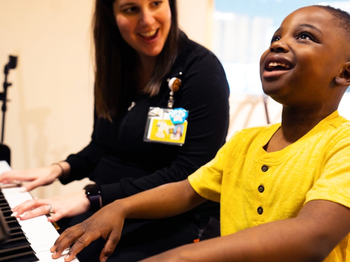 yellow shirt kid looking up very happy wearing playing piano with employee with white shirt 