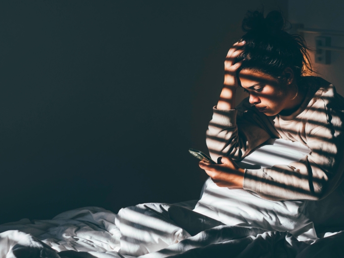 woman in dark room holding head window blinds shadow on her
