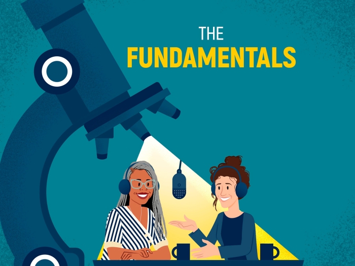 The Fundamentals with hosts Kelly Malcom and Jordan Goebig sitting on a microscope stage under a spotlight from the objective lenses.