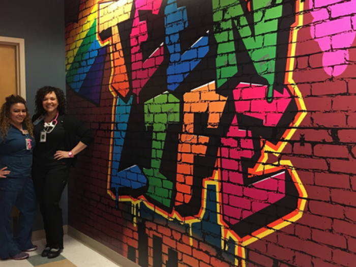 A picture of two health care professionals standing in front of a faux graffiti wall