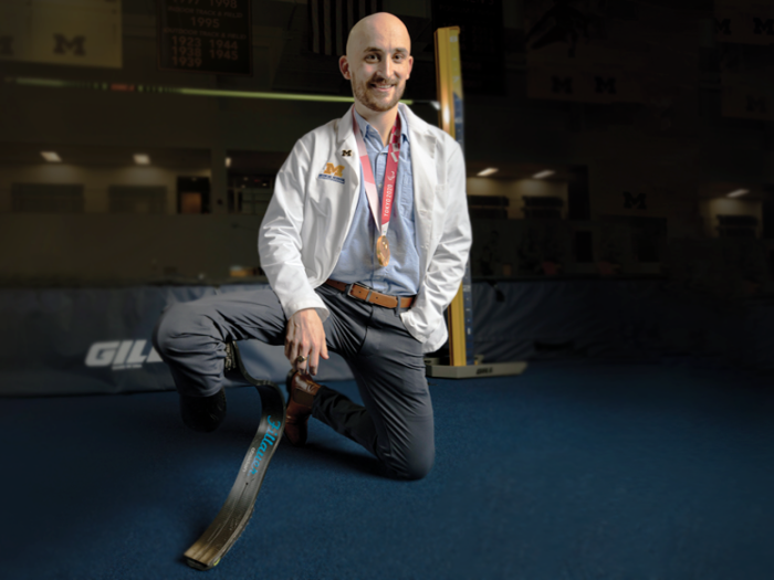 Man kneeling, wearing a doctor's white coat. His right leg has a prosthetic. 