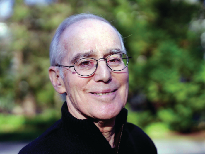 Close-up portrait of an older white man with gray hair and glasses. He outdoors and smiling.