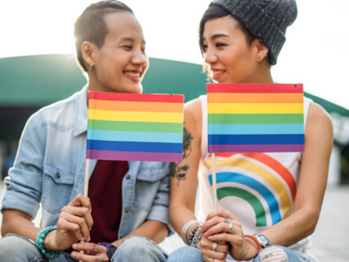 Stock photo of two young people are sitting outside holding Pride flags