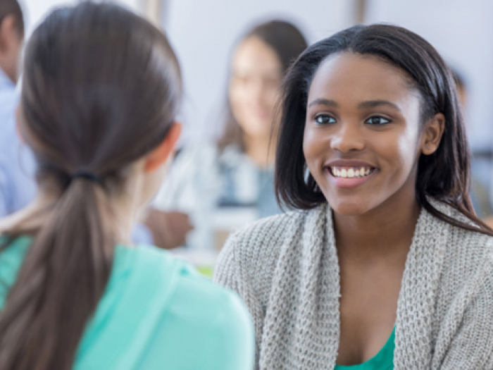 Two girls smiling and talking to each other.