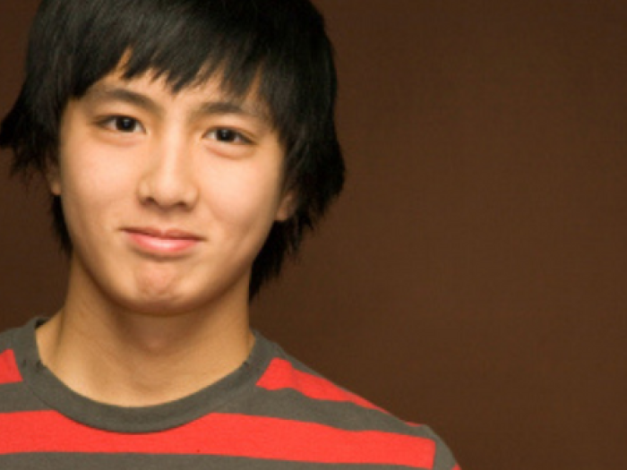 A boy wearing red and gray t-shirt smiles for the camera.