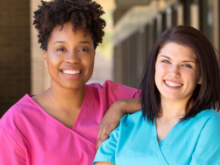 Two female providers in scrubs smile for a photo outside