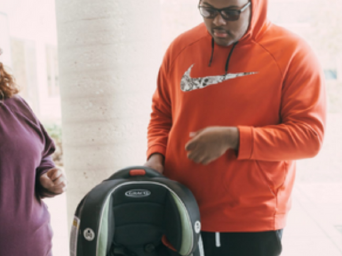 young man holds a car seat and speaks with a woman