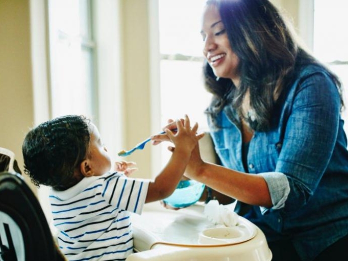child in a highchair being fed by their mother