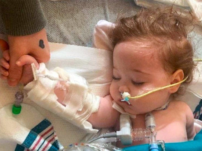 Baby sleeping in hospital bed with tubes holding moms hand