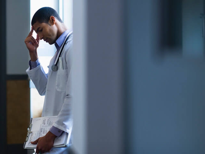 Doctor leaning against desk with clipboard in dark room with anxiety