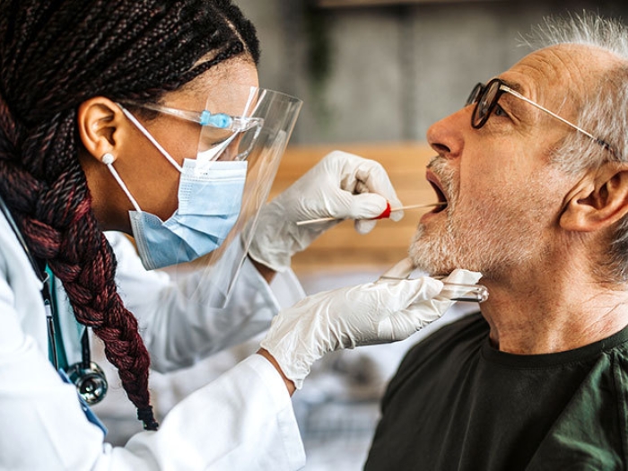 doctor swabs man's mouth with mask and eye glass gear on