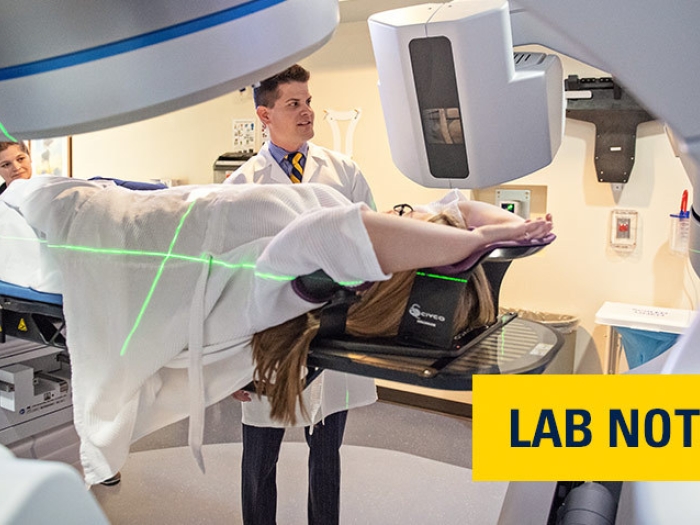 doctor in white coat scanning person in machine with words "lab note" written on yellow badge with blue font bottom right