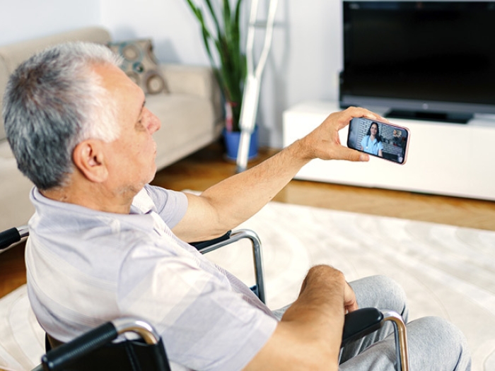man in wheel chair talking to doctor on smart phone in living room