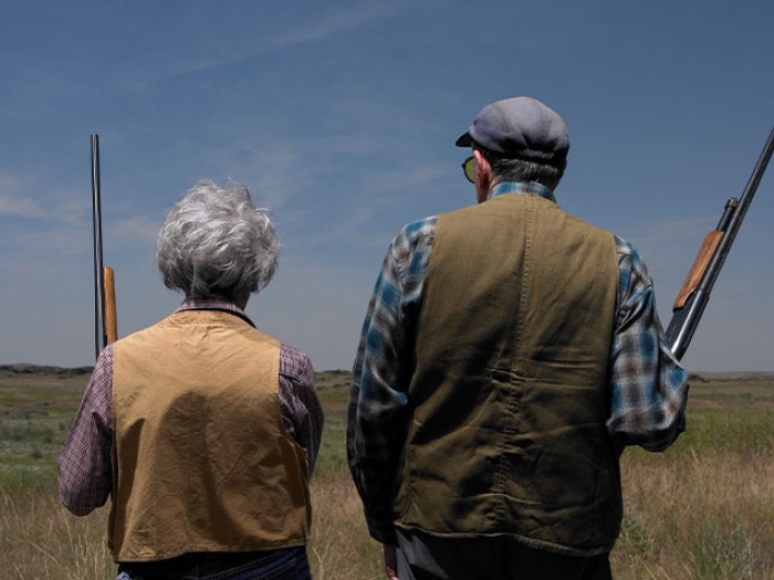 older couple in field holding shot guns