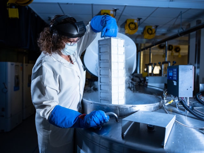 person lifting samples in biorepository with blue gloves, white coat and mask and goggles on