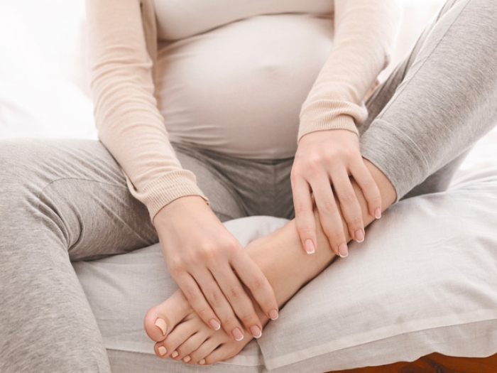 pregnant person holding feet on bed grey sweats