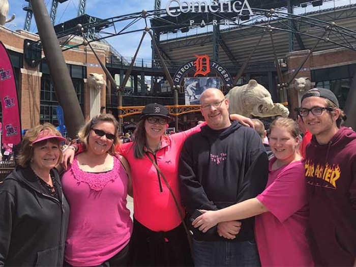 Group in pink, purple and black clothing celebrating, Detroit Tigers Comerica Park in background.
