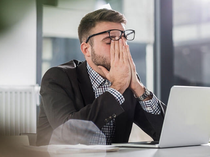 Tired man with hands on face leaning on desk while at work