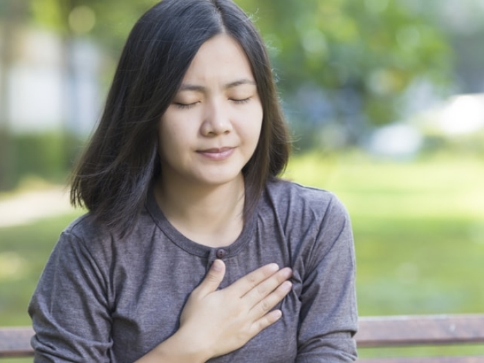 woman holding chest with hand sitting on park bench