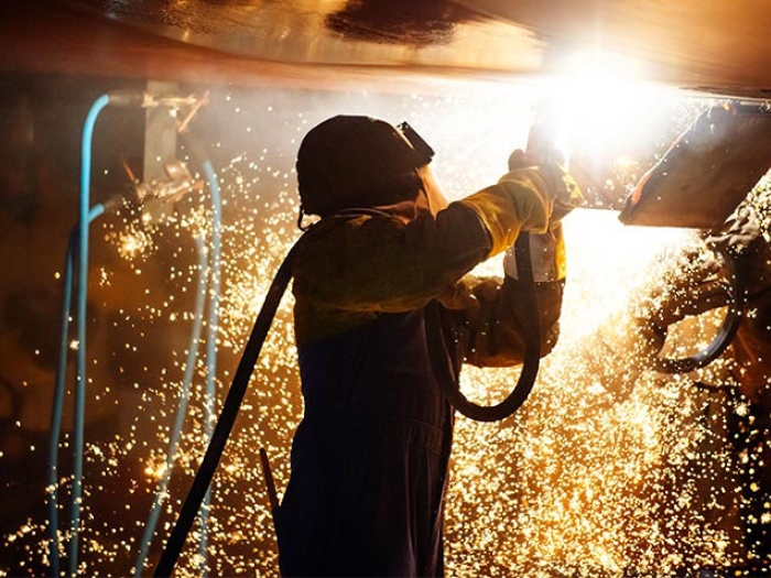 Person welding wearing coveralls and helmet sparks cascading