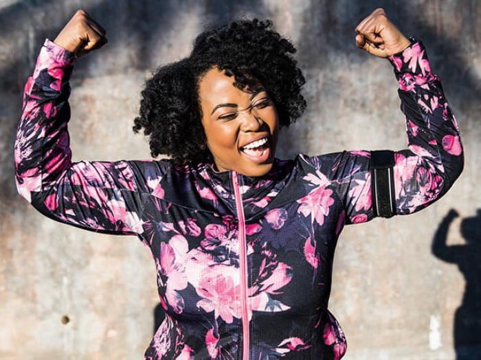 Woman in mauve zip up sports jacket with arms raised smiling