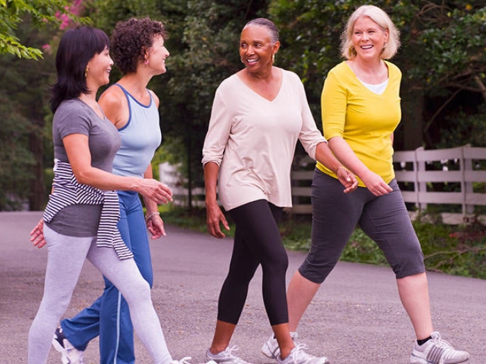 Four women walking outdoors on trail smiling
