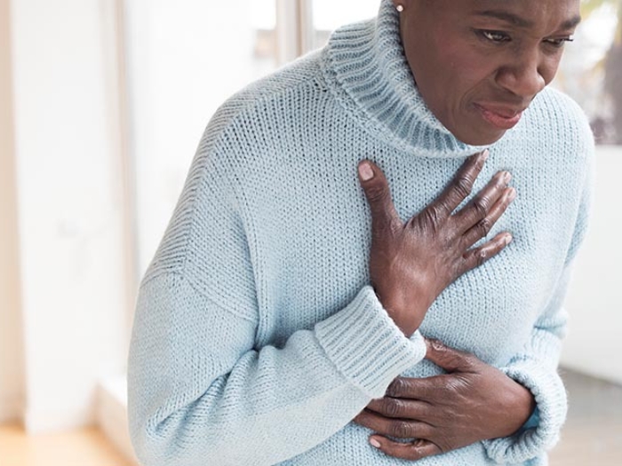 Woman bent over holding chest in light blue sweater.