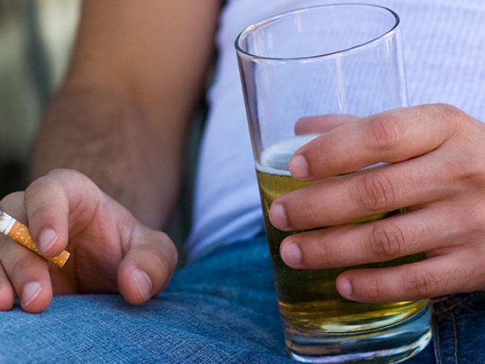 person closeup on lap holding cigarette and beer