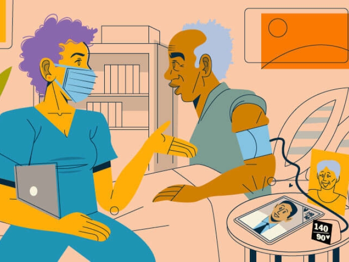 Provider in mask and scrubs sitting on edge of bed talking to patient.