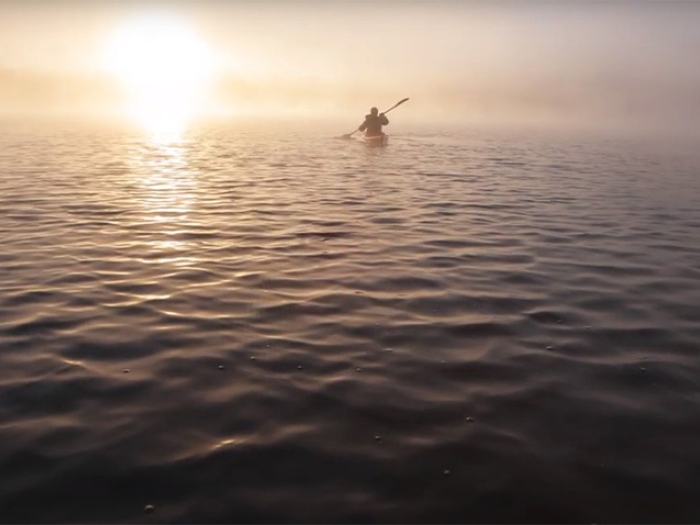 man paddling in boat on open water with sun