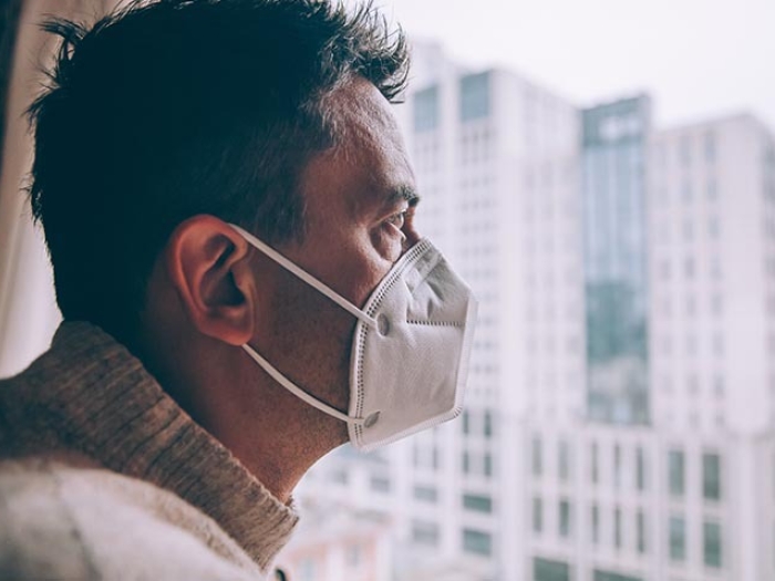 Man with mask on staring outside the window looking at city.